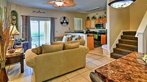 A living room with a sofa, a coffee table, a ceiling fan, and a kitchen area with cabinets and a microwave. - Gorgeous 4bd/3ba Reunion Resort Near Disneyland (Kissimmee)
