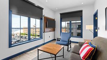 A modern living room with large windows, a flat-screen TV, a sofa, and a coffee table.