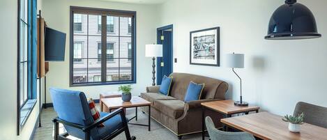 A modern living room with a sofa, chairs, a dining table, and a large window offering a city view.