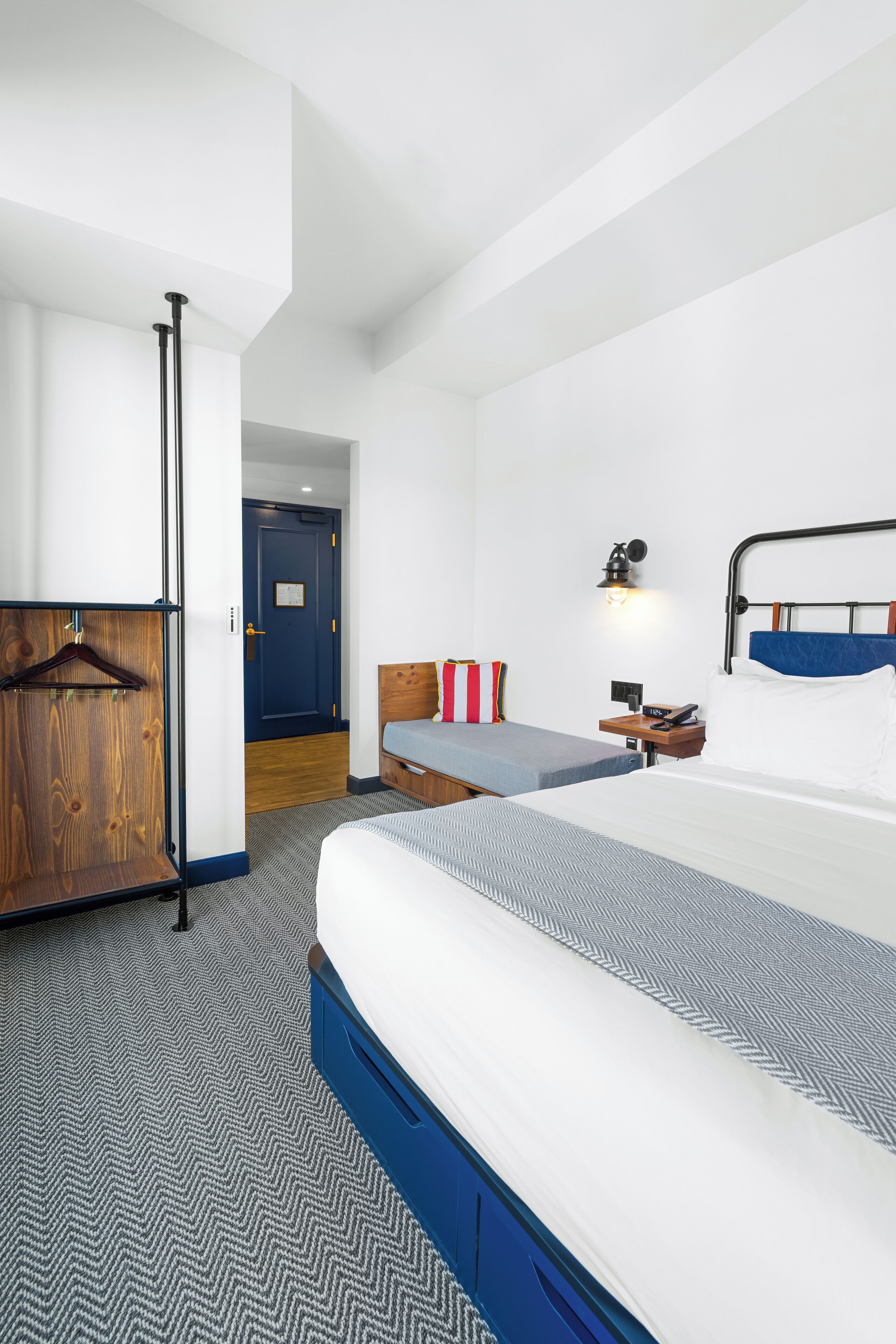 A hotel room with a large bed, a bedside table, a wardrobe, and a door leading to another room.
