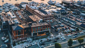 A marina with numerous boats docked, a bridge in the background, and a parking lot with cars.