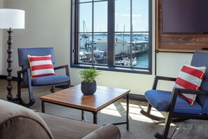 A room with two blue armchairs, a wooden coffee table, a lamp, and a view of a marina through large windows. - Hammetts Hotel (Newport)