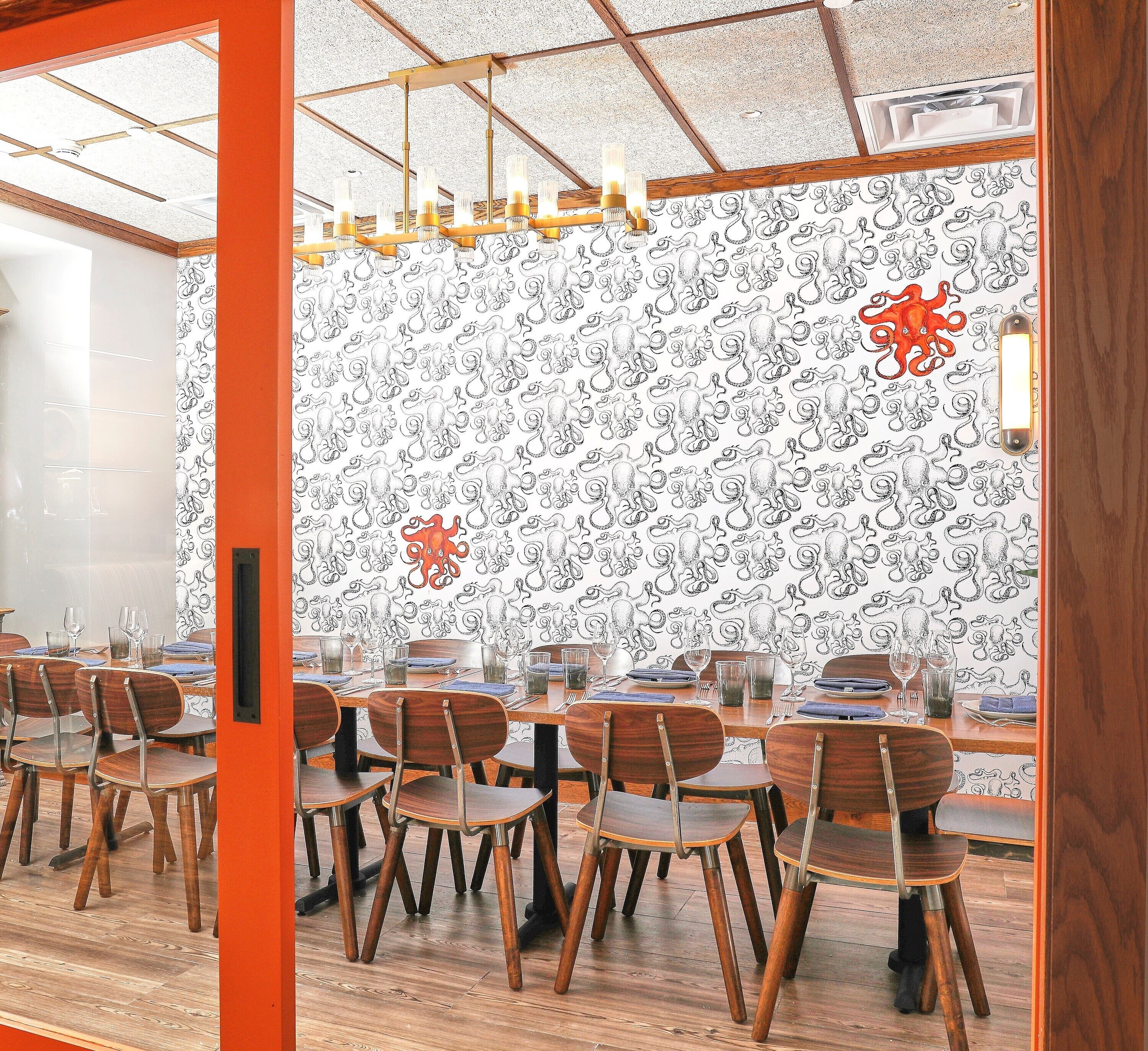 A conference room with wooden chairs and tables, a patterned wall, and a ceiling with a grid design and hanging lights.