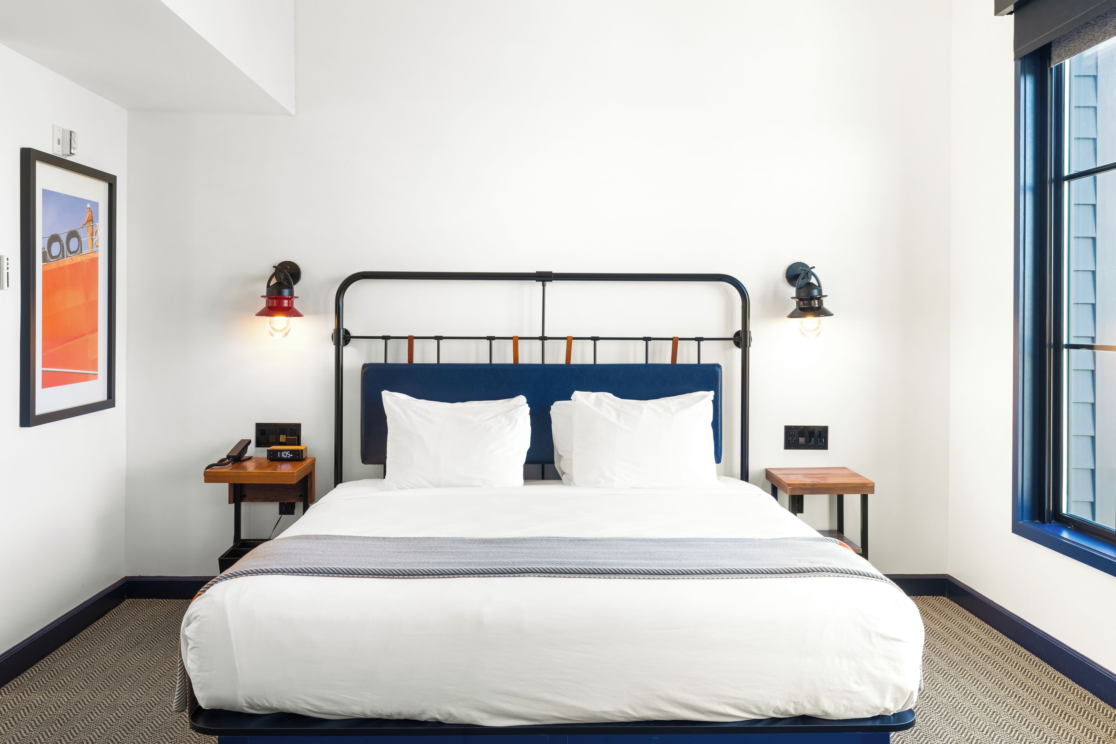 A neatly made bed with white linens, a blue headboard, and two bedside lamps.