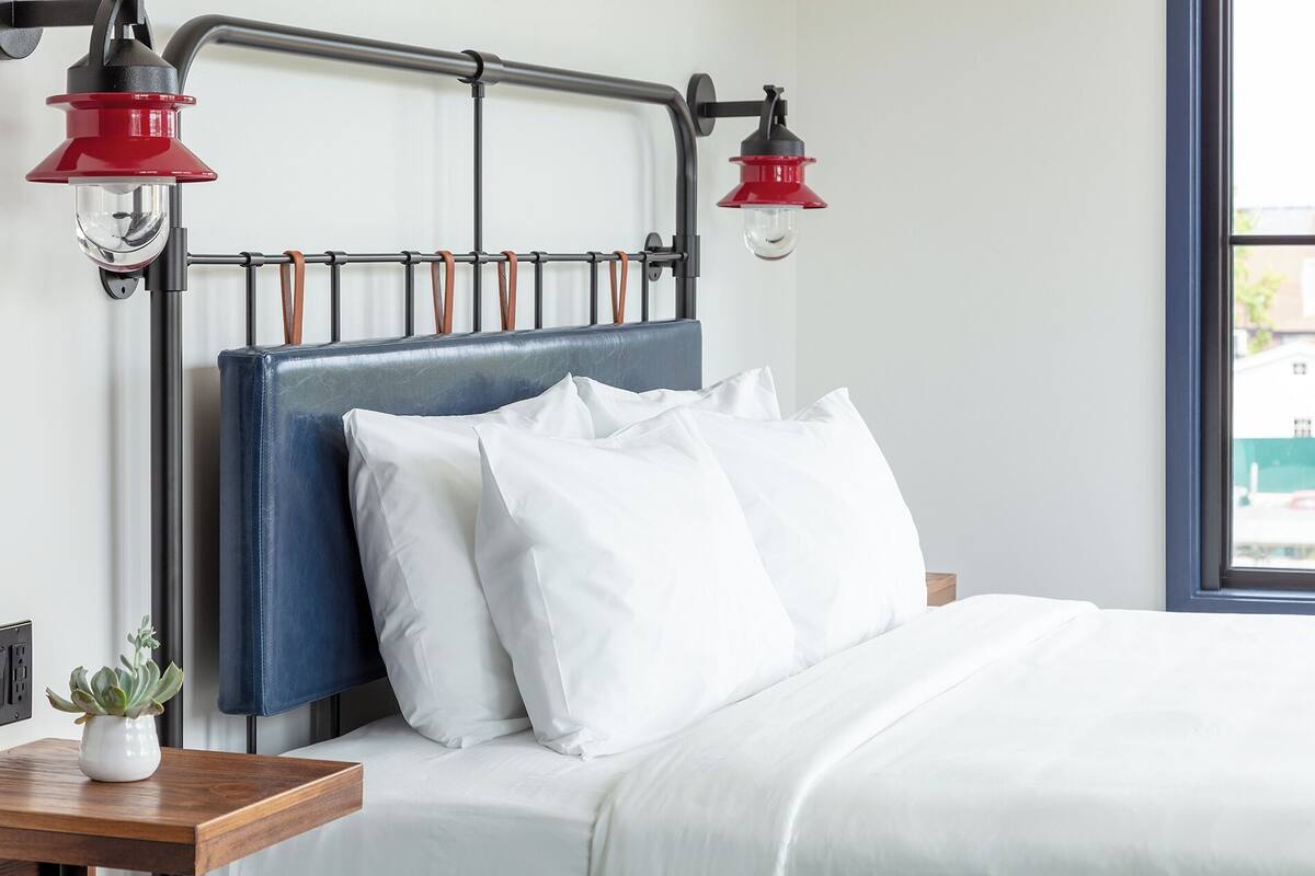 A bedroom with a blue headboard, white bedding, and two red wall-mounted lamps.