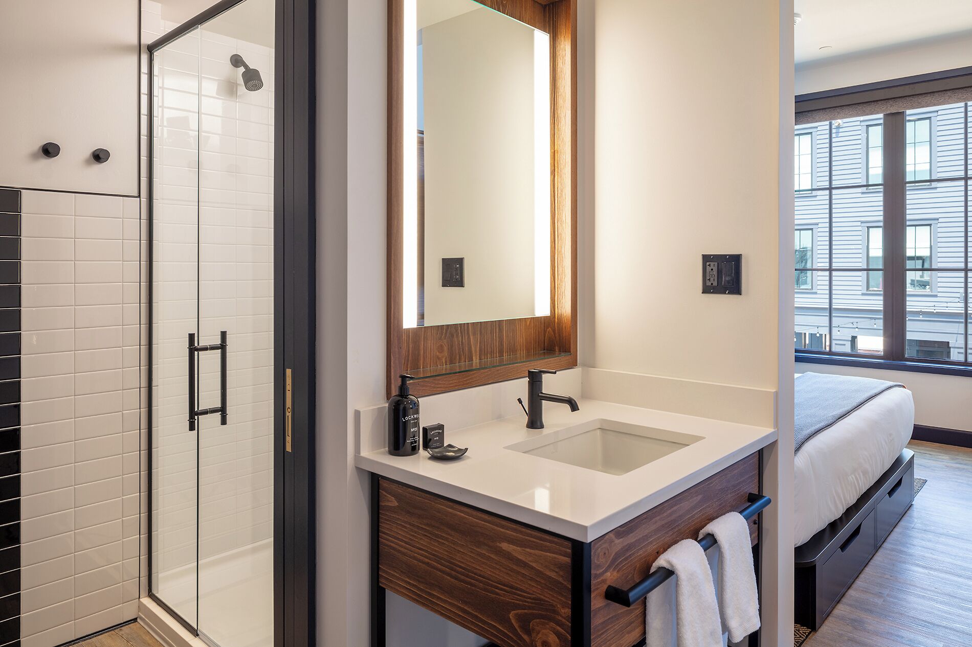 Une salle de bain moderne avec une douche à parois de verre, un grand miroir, un lavabo et un meuble-vasque en bois.