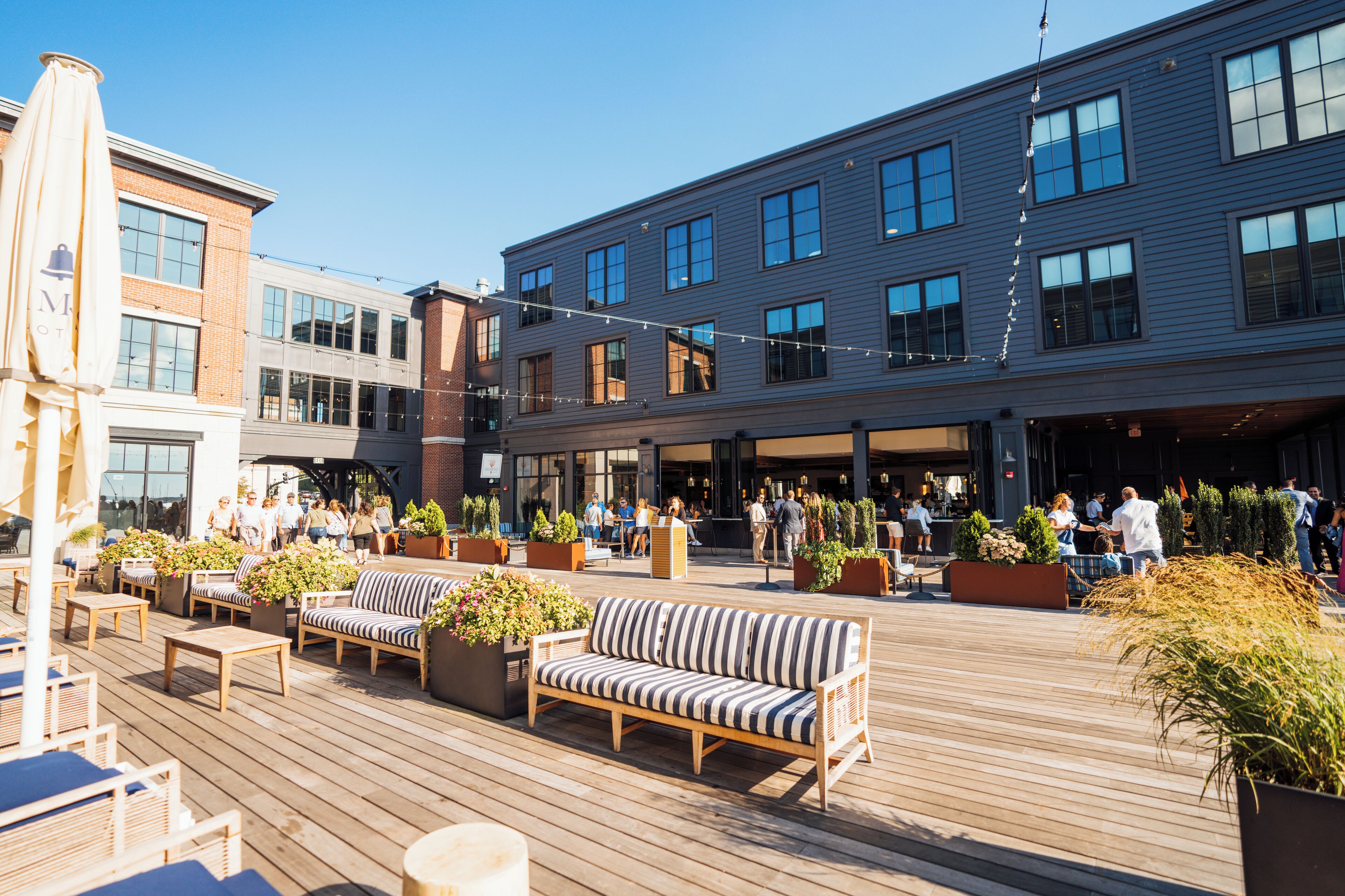 An outdoor deck with seating, potted plants, and a building with multiple windows and a balcony.