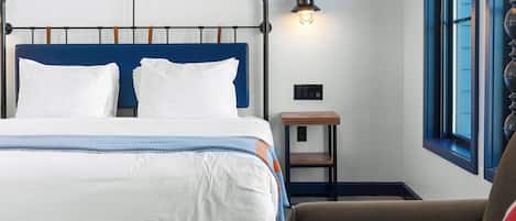 A hotel room with a bed, a nightstand, a lamp, and a window.