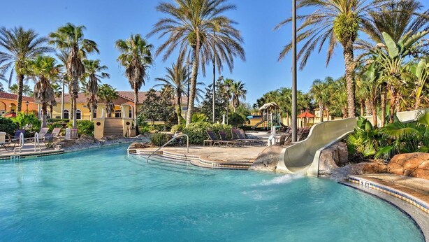 Une piscine avec un toboggan, entourée de palmiers et de chaises longues.