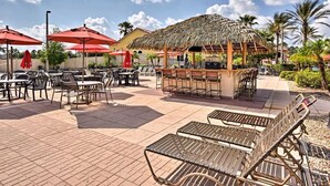 Un espace extérieur aménagé en terrasse, avec des tables et des chaises, un bar et une structure dotée d’un toit de chaume.