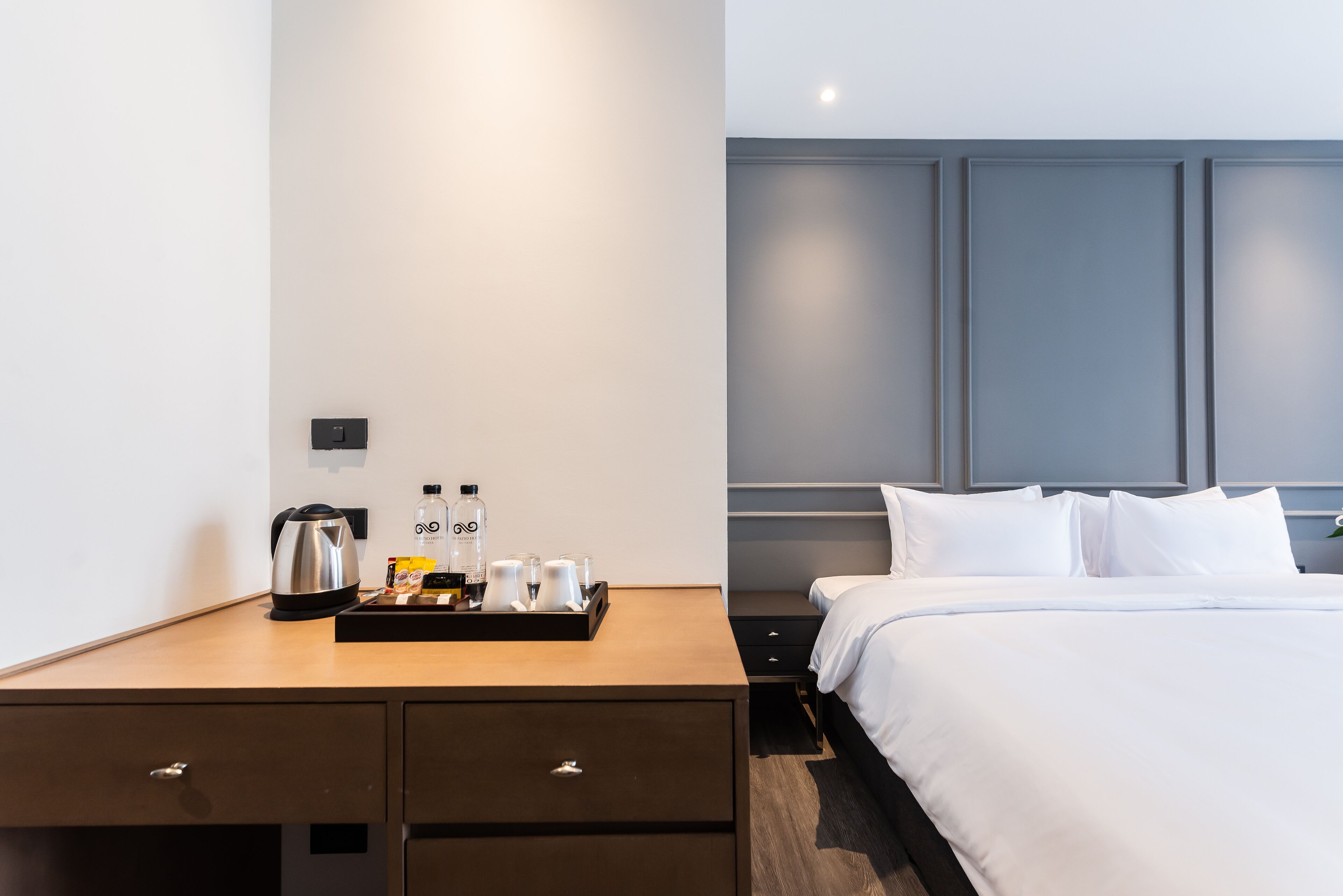 Habitación de hotel con un escritorio de madera, una cama con ropa blanca y una bandeja con café y alimentos para el desayuno.