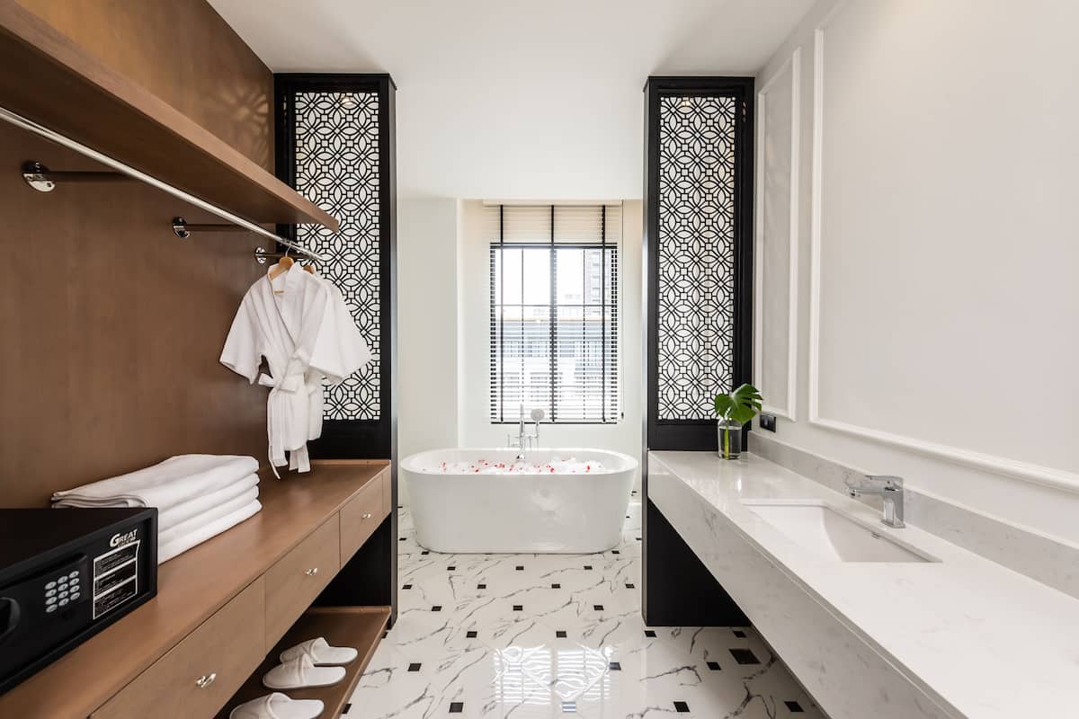 Un baño moderno con una bañera independiente, un tocador con un espejo grande, y un mueble de madera con toallas y zapatillas.