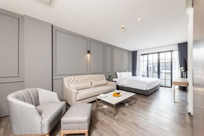 A modern hotel room with a grey sofa, a bed, a wooden coffee table, and a large window with a city view. - One Patio Hotel Pattaya (Pattaya)