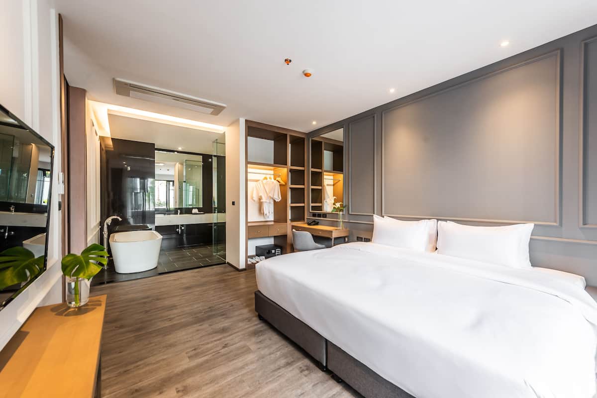 Una habitación de hotel moderna con una cama grande, un escritorio integrado, un vestidor y un baño con ducha de vidrio.