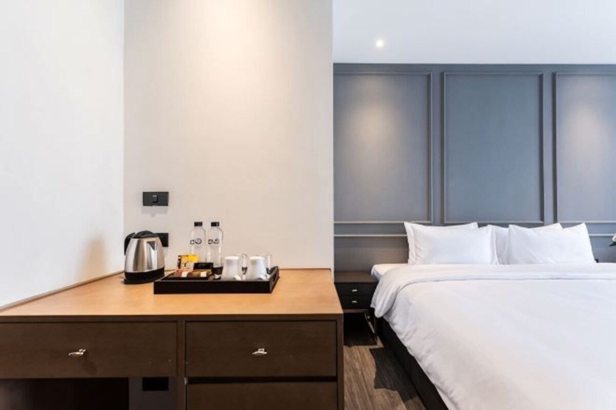 Ein Hotelzimmer mit Bett, Nachttisch mit Ablage für Annehmlichkeiten, Nachtlicht und Wandlampe.