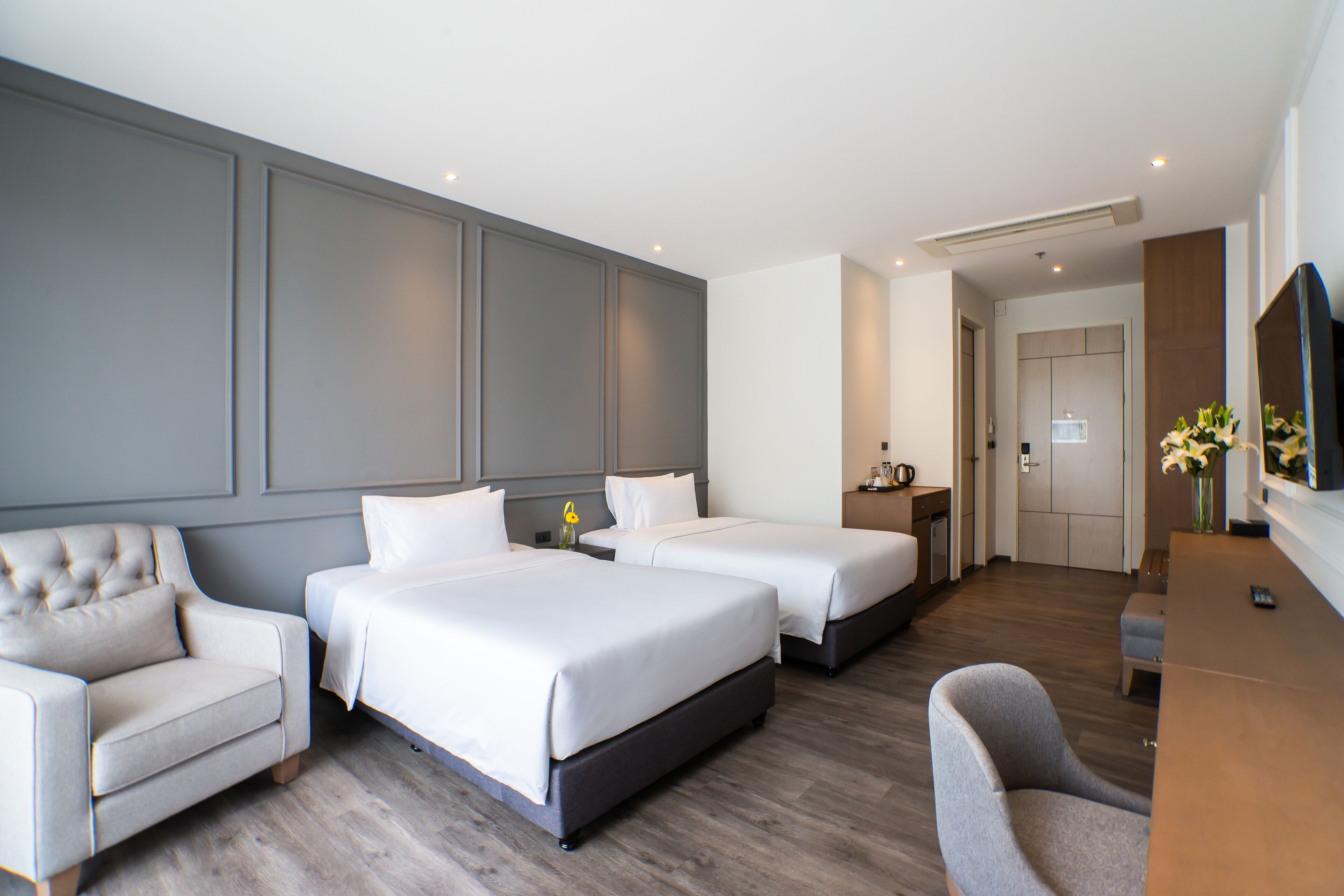 A hotel room with two beds, a sofa, a desk, and a TV.