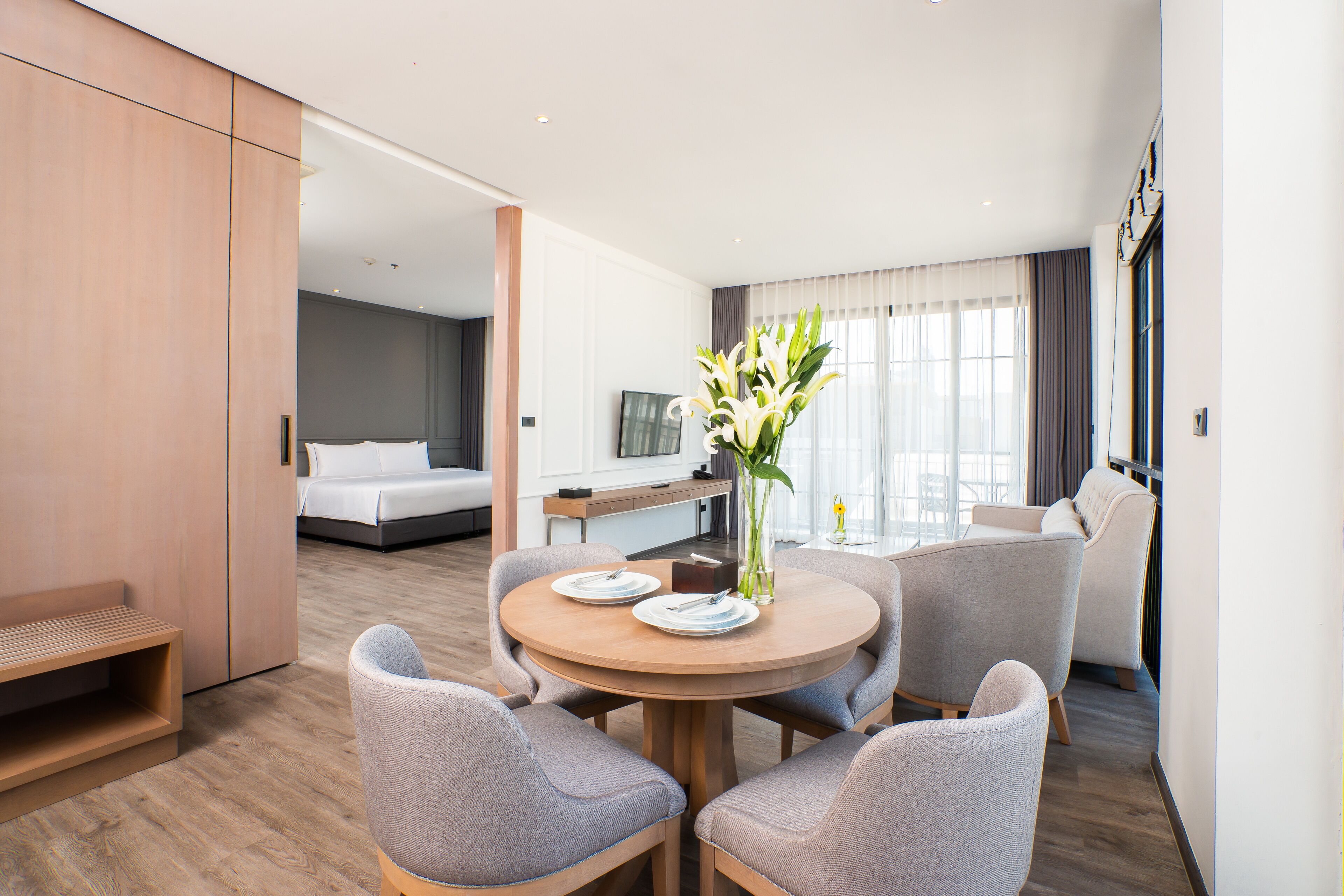 Una habitación de hotel con cama, escritorio, silla, una mesa redonda y un florero con flores.