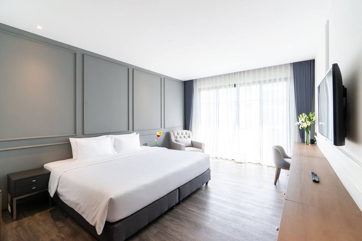 A modern hotel room with a large bed, a desk, and a TV mounted on the wall.