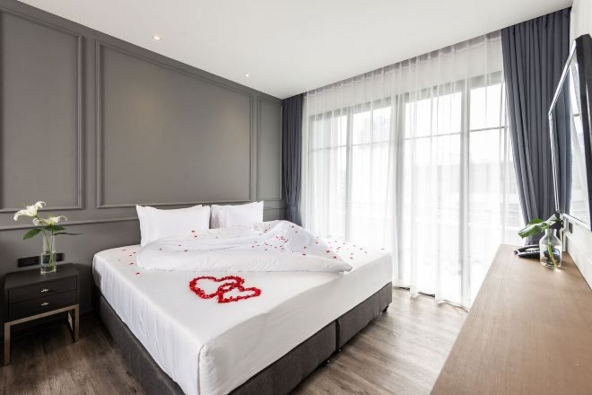 Ein modernes Hotelzimmer mit einem großen Bett, einem Nachttisch und einem Fenster mit Vorhängen.