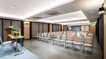 Un salón de conferencias con filas de sillas, un atril adornado con flores y un diseño de techo moderno.