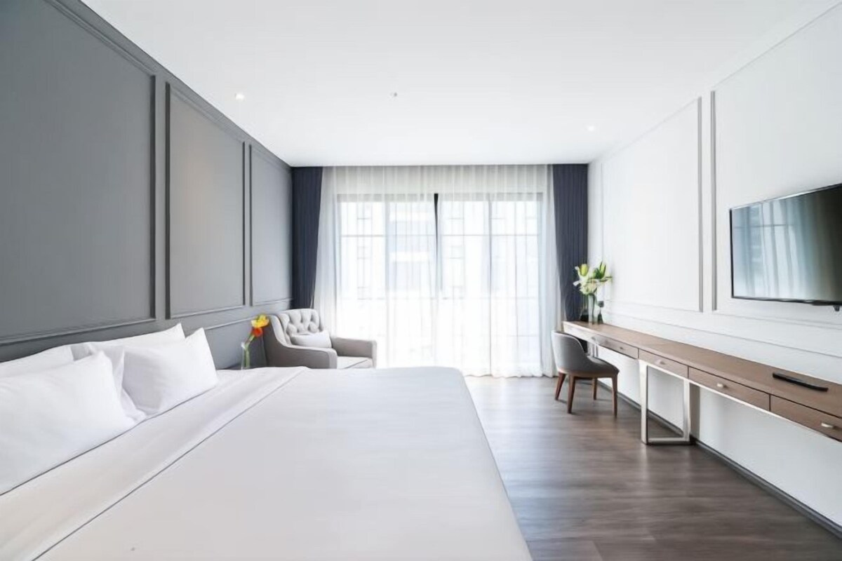A modern hotel room with a large bed, a desk, a chair, and a TV.