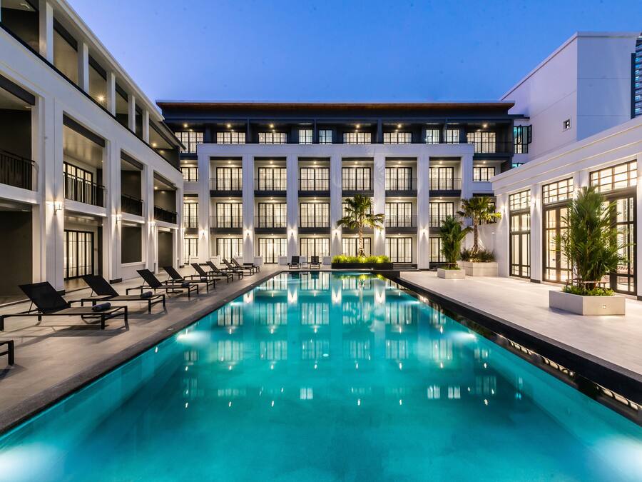 Un hotel moderno con piscina, tumbonas y fachada bien iluminada.