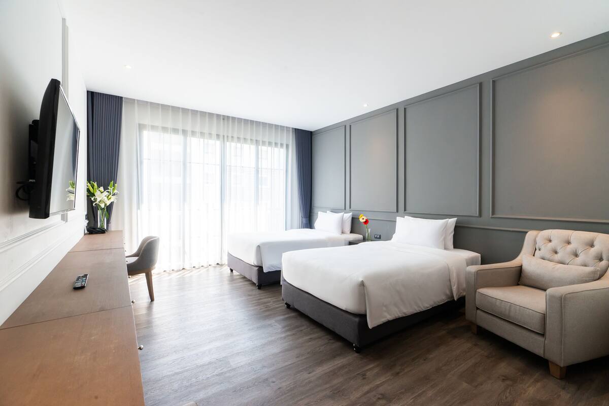 A hotel room with two beds, a sofa, a TV, and a desk.