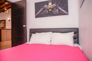 Une chambre à coucher avec un lit, une tête de lit sombre et un tableau accroché au mur.