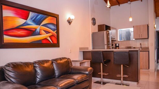 Ein modernes Wohnzimmer mit einer Ledersofa, einem großen abstrakten Gemälde und einer Küchenzeile mit Bar.