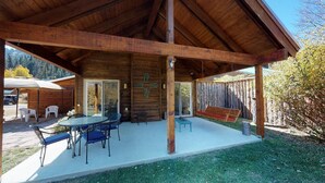 A covered outdoor patio with a wooden table and chairs, a bench, and a view of the surrounding area.