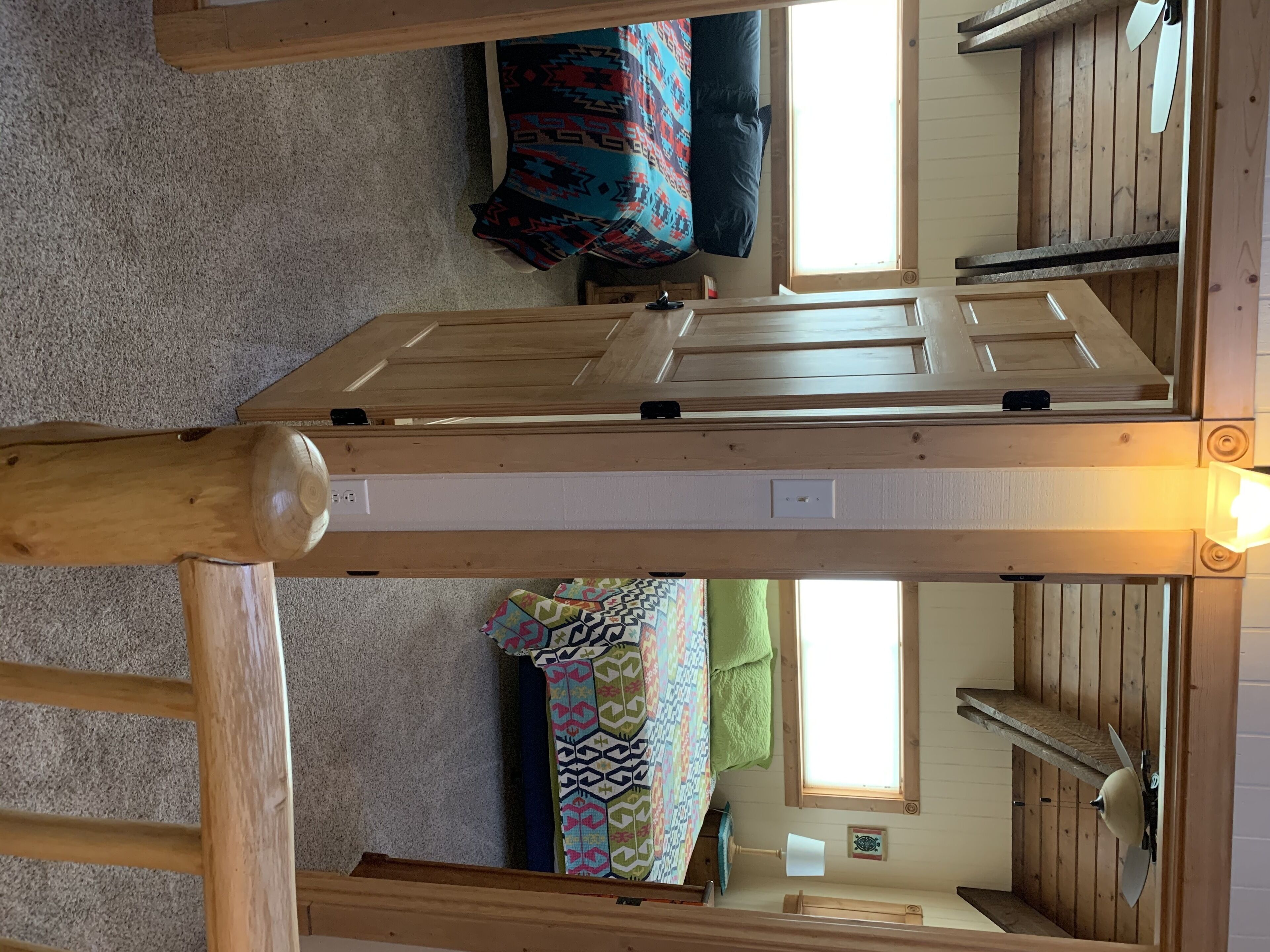 A room with a wooden bed frame, a patterned bedspread, a green towel, and a window with a view of the outside.