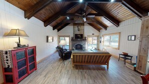 A spacious room with a fireplace, wooden beams, a sofa, and a dining table.