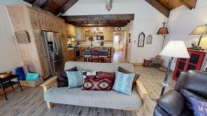 A cozy living room with a sofa, a dining table, and a kitchen in the background.