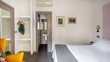 A hotel room with a bed, a chair, a wardrobe, a sink, and two framed pictures on the wall.