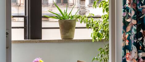 A balcony with a wooden table and chairs, a potted plant, and a view of a building with stone walls and windows.