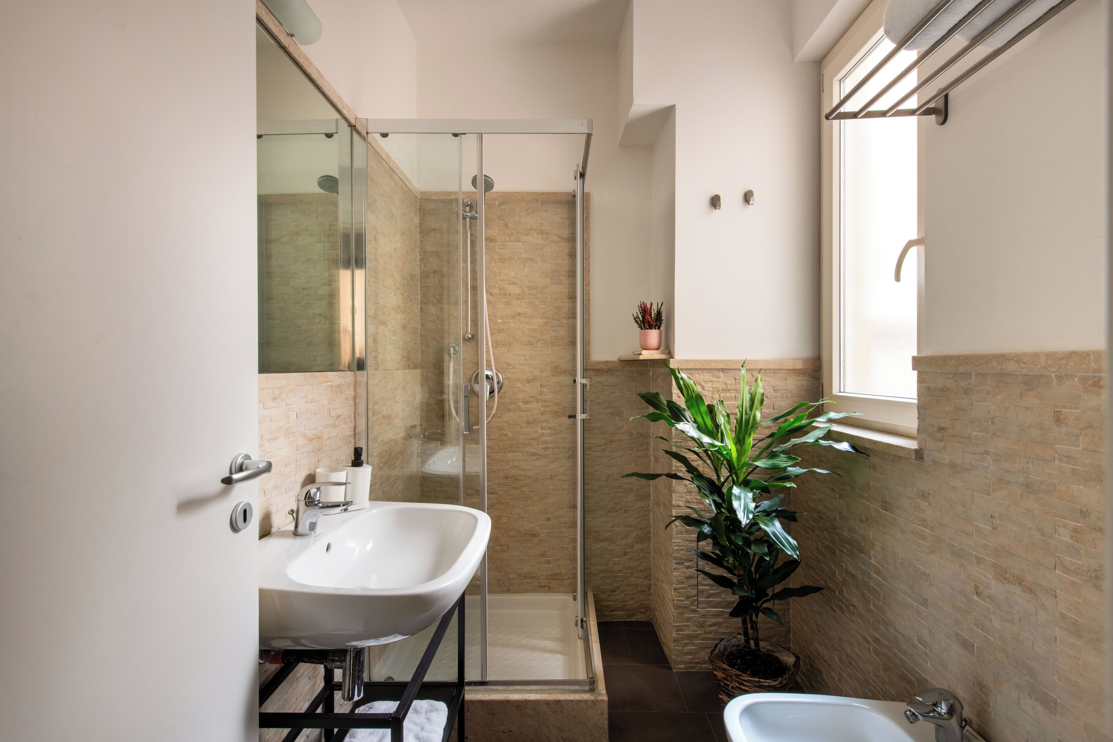 A modern bathroom with a freestanding bathtub, a glass-enclosed shower, and a potted plant.