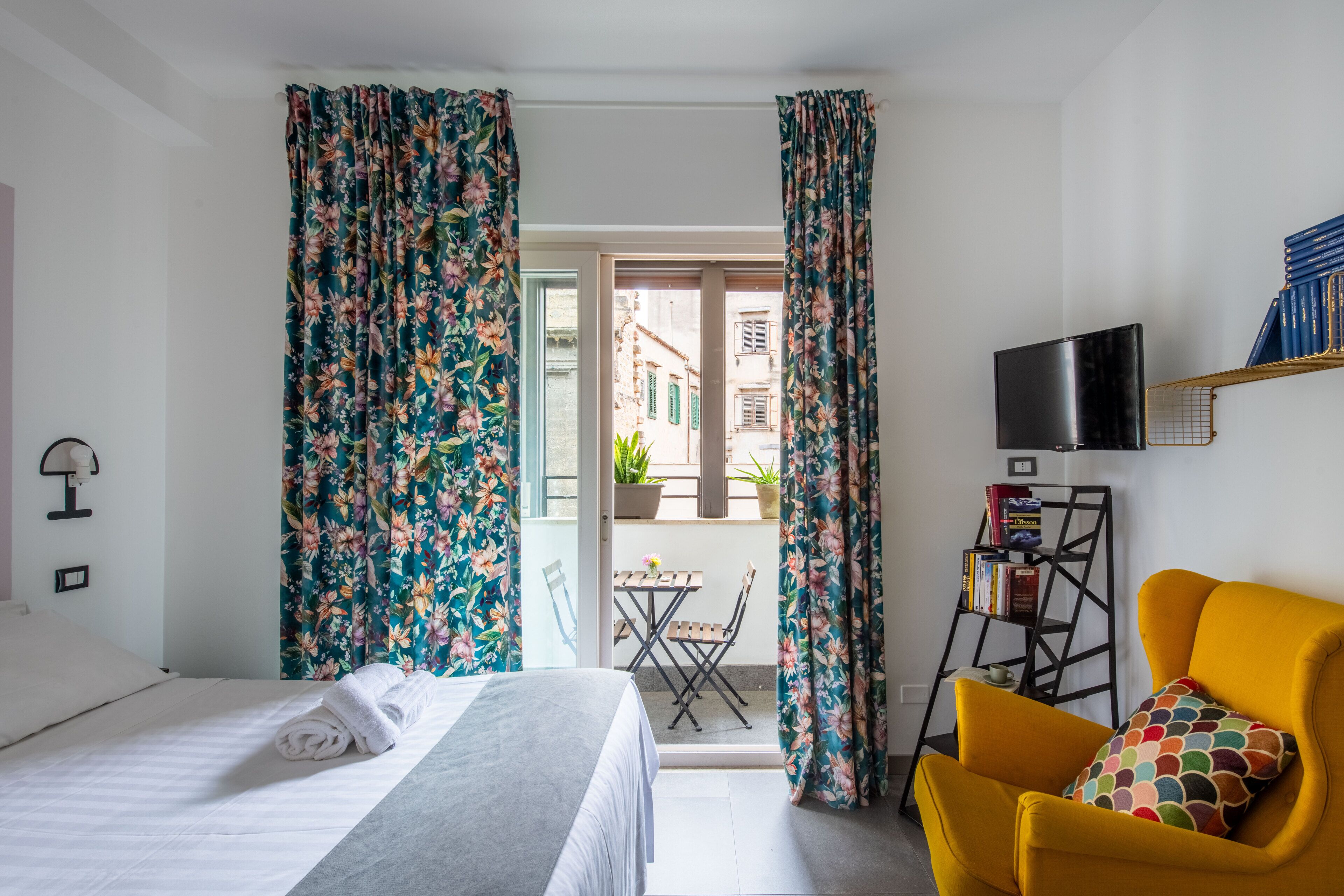 Una habitación de hotel con una cama, un sillón amarillo, un televisor y una estantería.