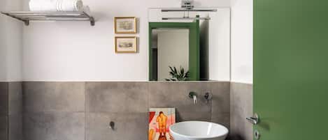 Un bagno con un lavandino bianco, uno specchio grande, un porta asciugamani e una porta verde.