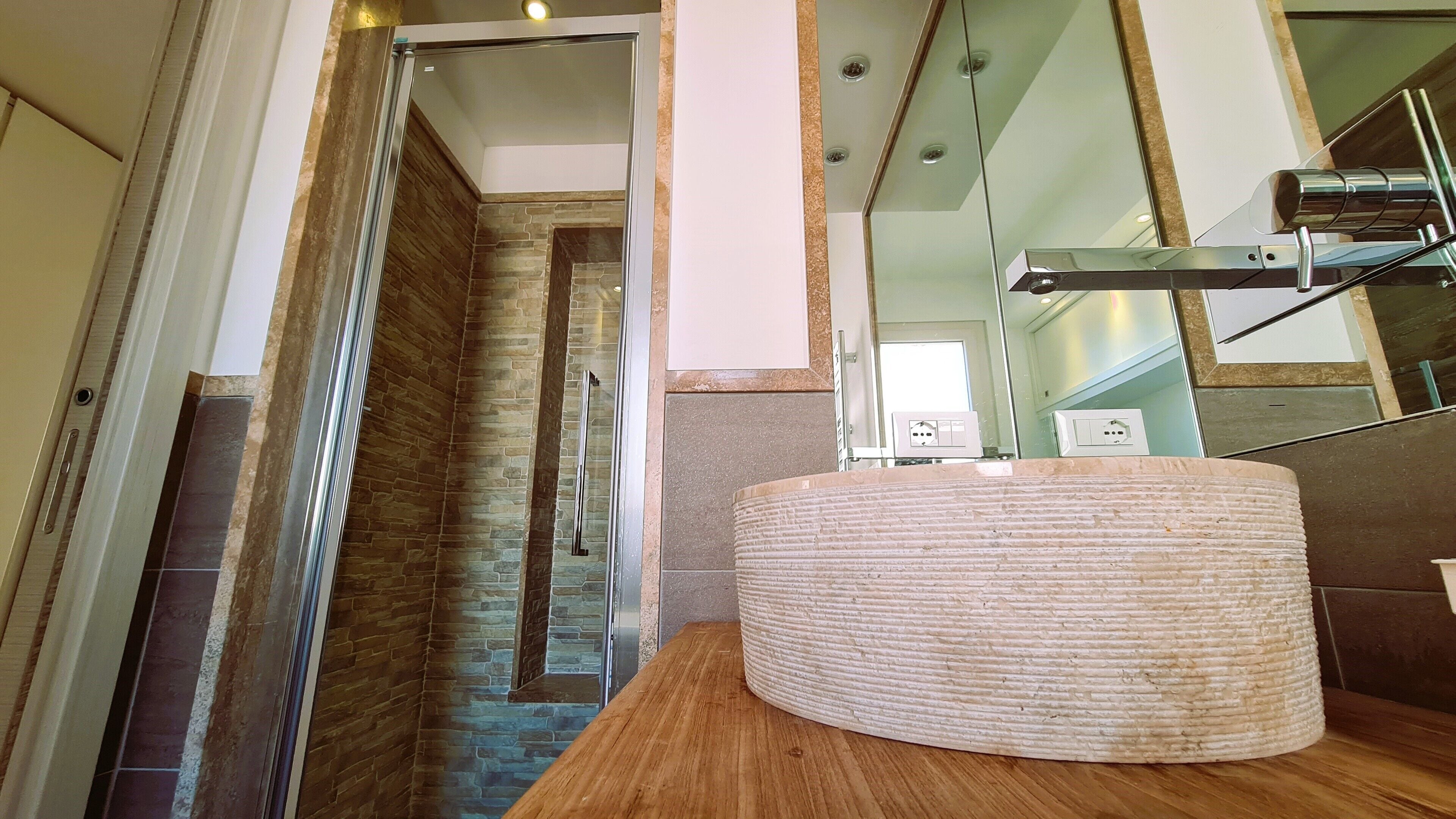 Une salle de bain moderne avec un mur en pierre, un meuble-lavabo en bois et un miroir.