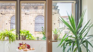 Un balcón con mesa lista para comer, rodeado de plantas en macetas y vista a un edificio histórico.