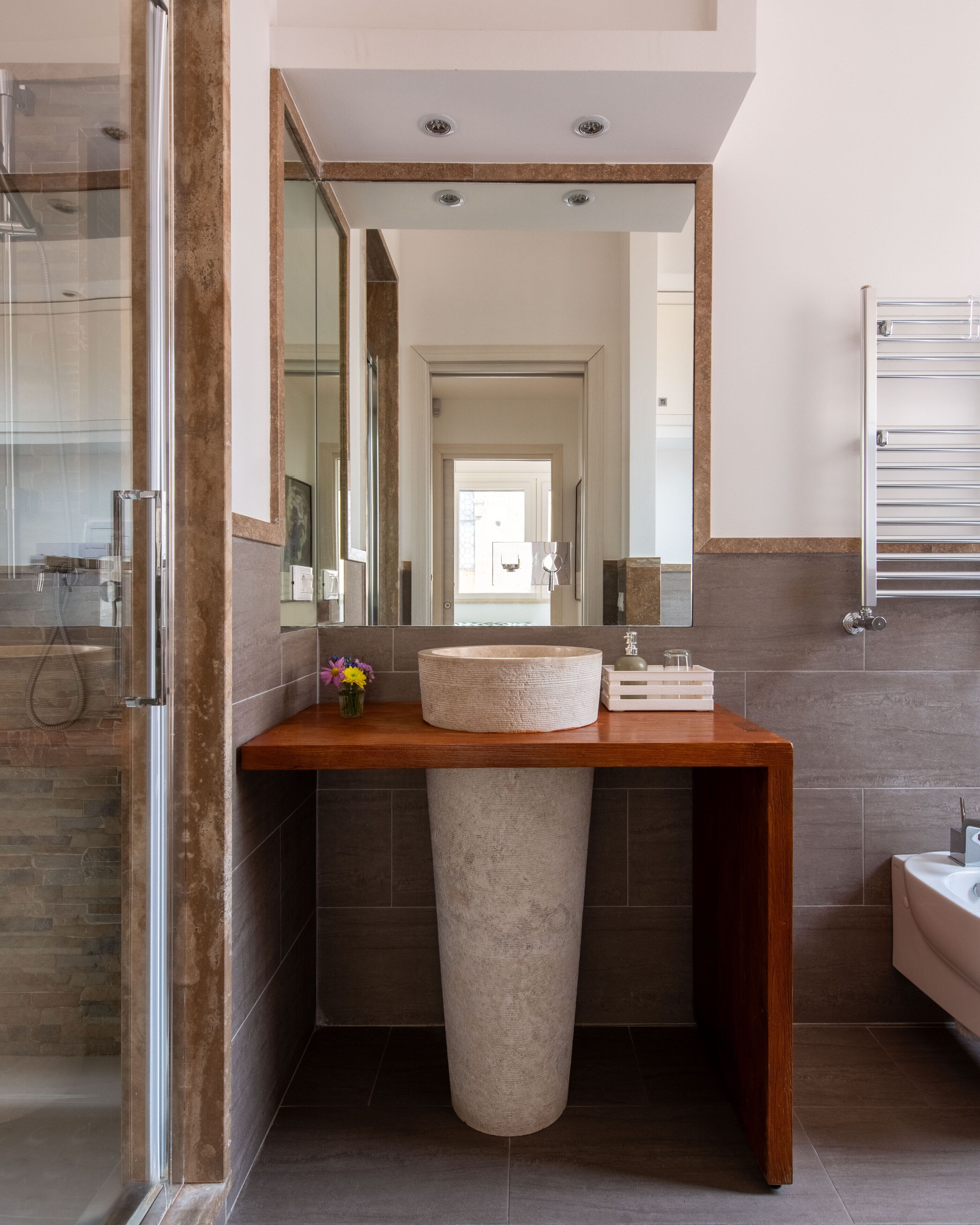 A modern bathroom with a large mirror, a stone sink, and a shower area.