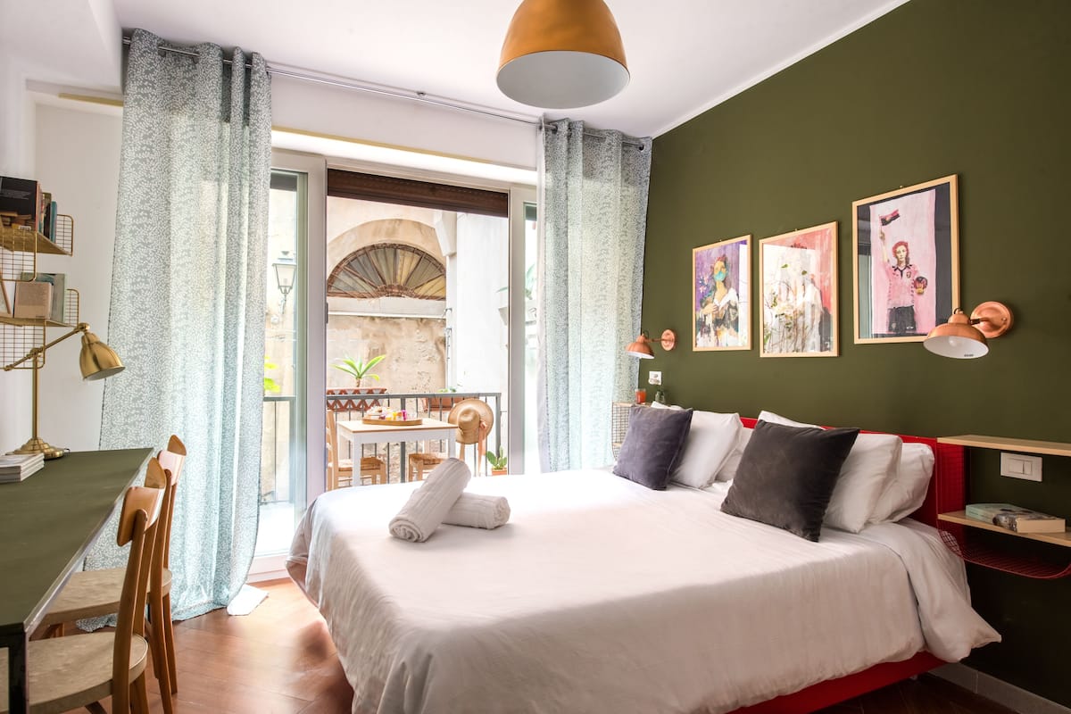 A modern hotel room with a large bed, a desk, and a balcony with a view.