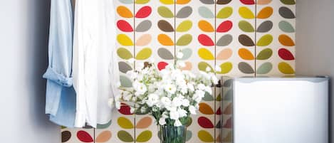 A room with a patterned wallpaper, a white appliance, and a vase with white flowers on a table.