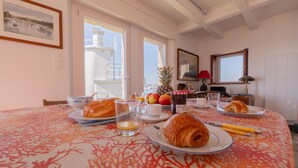 A dining table with breakfast items, a pineapple, and a view of the sea through large windows.