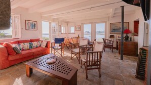 A spacious living area with a red sofa, wooden chairs, a coffee table, and a stone floor.