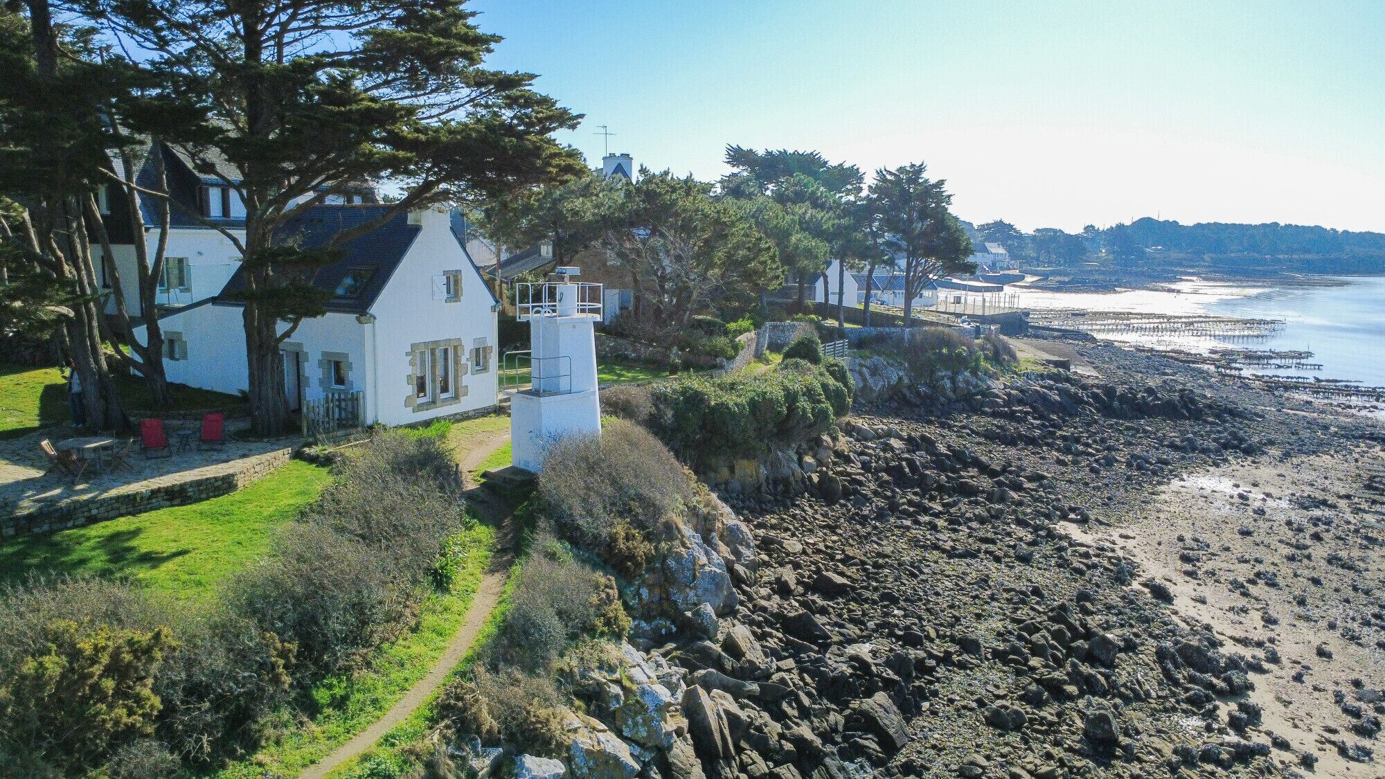 Ein Küstenhaus mit Leuchtturm, felsigem Strand und freiem Blick aufs Meer.