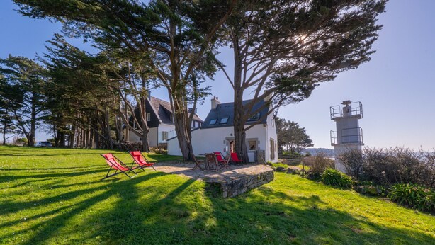 A house with a stone patio, red chairs, and a lighthouse in the background.