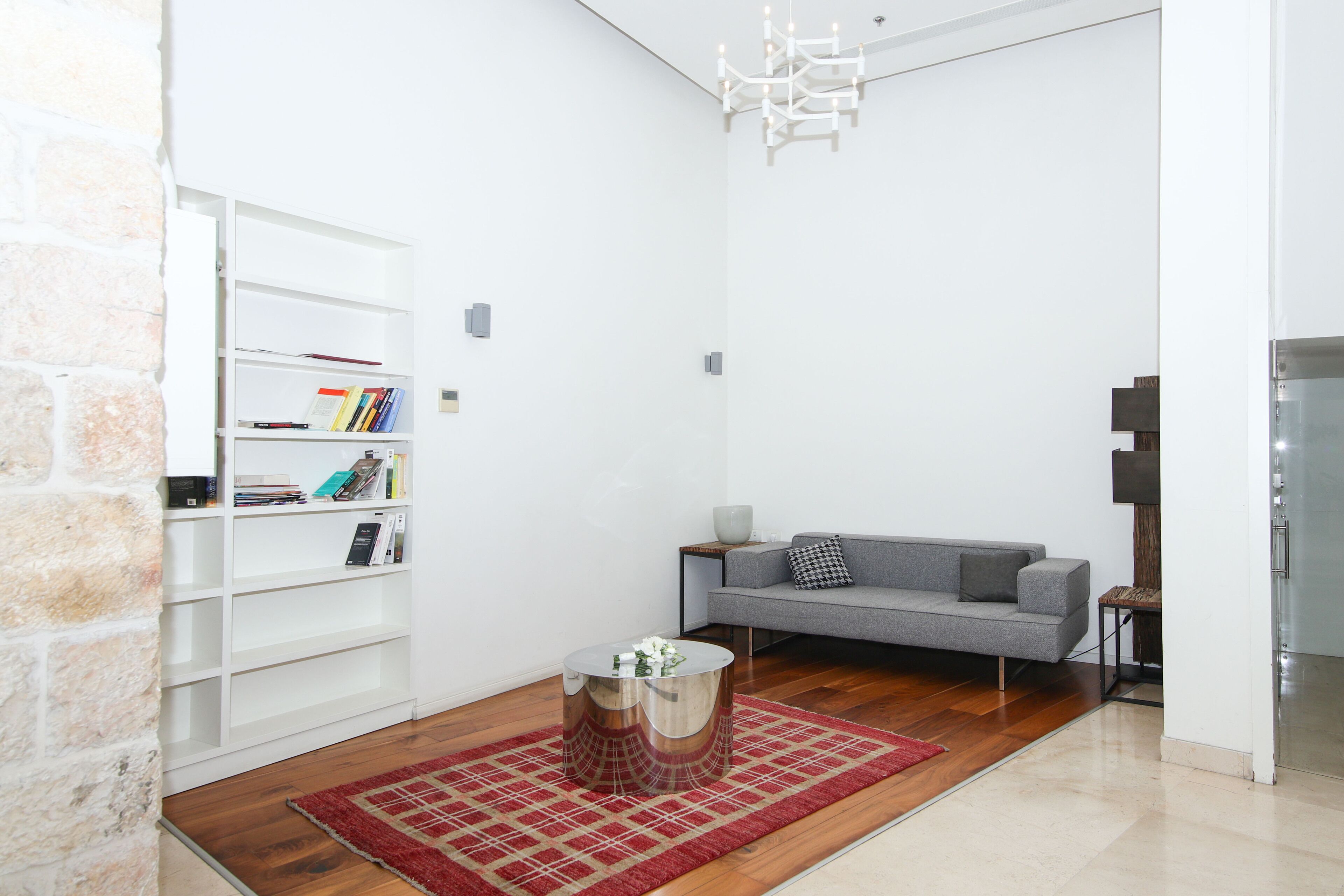 A modern living room with a bookshelf, a grey sofa, a red rug, and a chandelier.