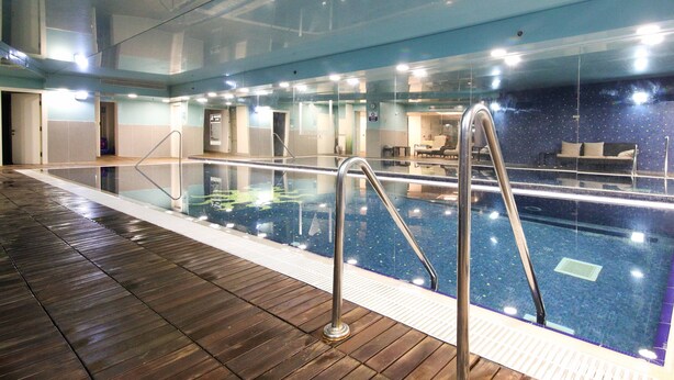 Una piscina interior con paredes de vidrio transparente, suelo de madera y barandillas de metal.