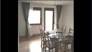 A dining area with a wooden table set for four, two windows with curtains, and a light fixture above. - FeWo BC 40 (Stuttgart)